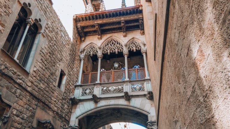 Neo-Gothic Bishop’s Bridge crossing Carrer del Bisbe in Barcelona’s Gothic Quarter, with ornate stonework and pointed arches.
