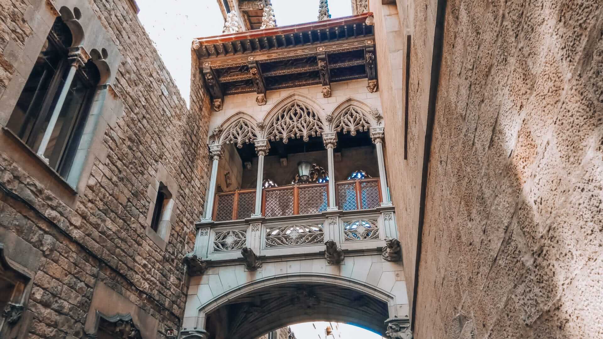 Neo-Gothic Bishop’s Bridge crossing Carrer del Bisbe in Barcelona’s Gothic Quarter, with ornate stonework and pointed arches.