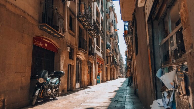 Quiet street view of Carrer de la Mercè in Barcelona’s Gothic Quarter with a parked motorcycle, café signs, and balconies.