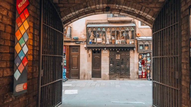 View from the arched entrance of Casa Padellàs toward Carrer del Veguer in Barcelona’s Gothic Quarter, with a historic façade and souvenir shop.