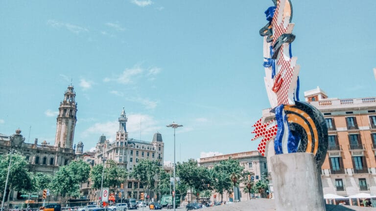 Roy Lichtenstein's colorful sculpture "El Cap de Barcelona" near Passeig de Colom with historic buildings in the background.