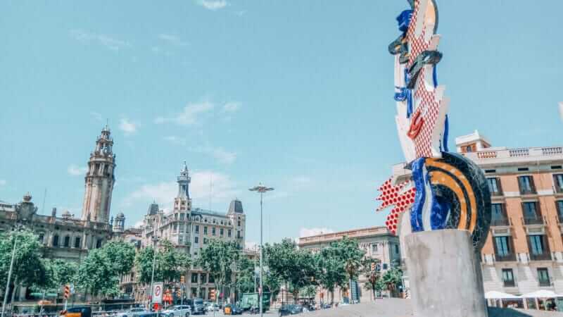 Roy Lichtenstein's colorful sculpture "El Cap de Barcelona" near Passeig de Colom with historic buildings in the background.