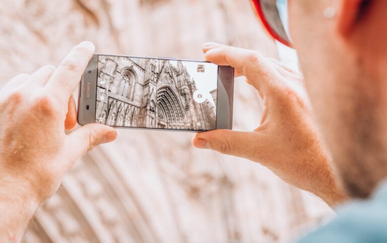 A person photographing the Neo-Gothic façade of the Barcelona Cathedral with a smartphone at Pla de la Seu in the Gothic Quarter.
