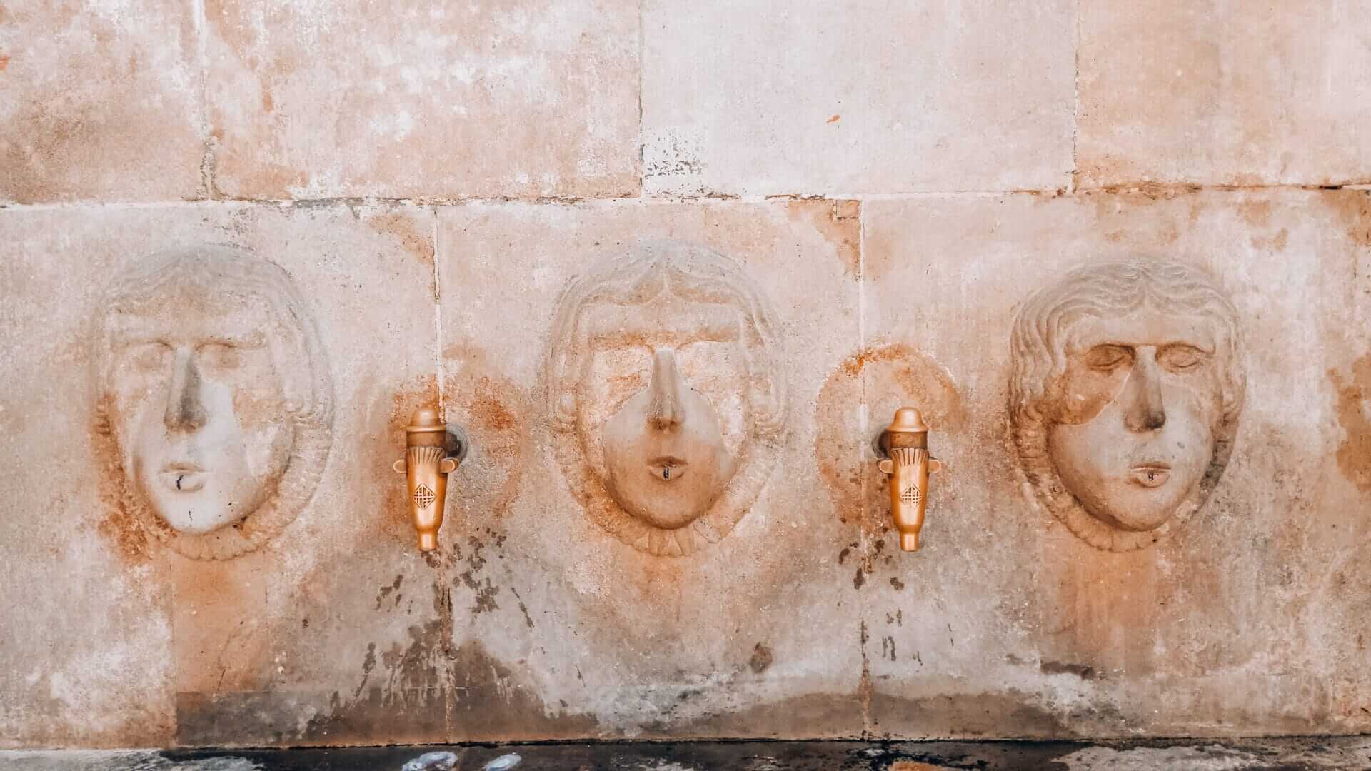 Historic stone drinking fountain with three carved faces in Plaça Sant Just, Gothic Quarter, Barcelona.
